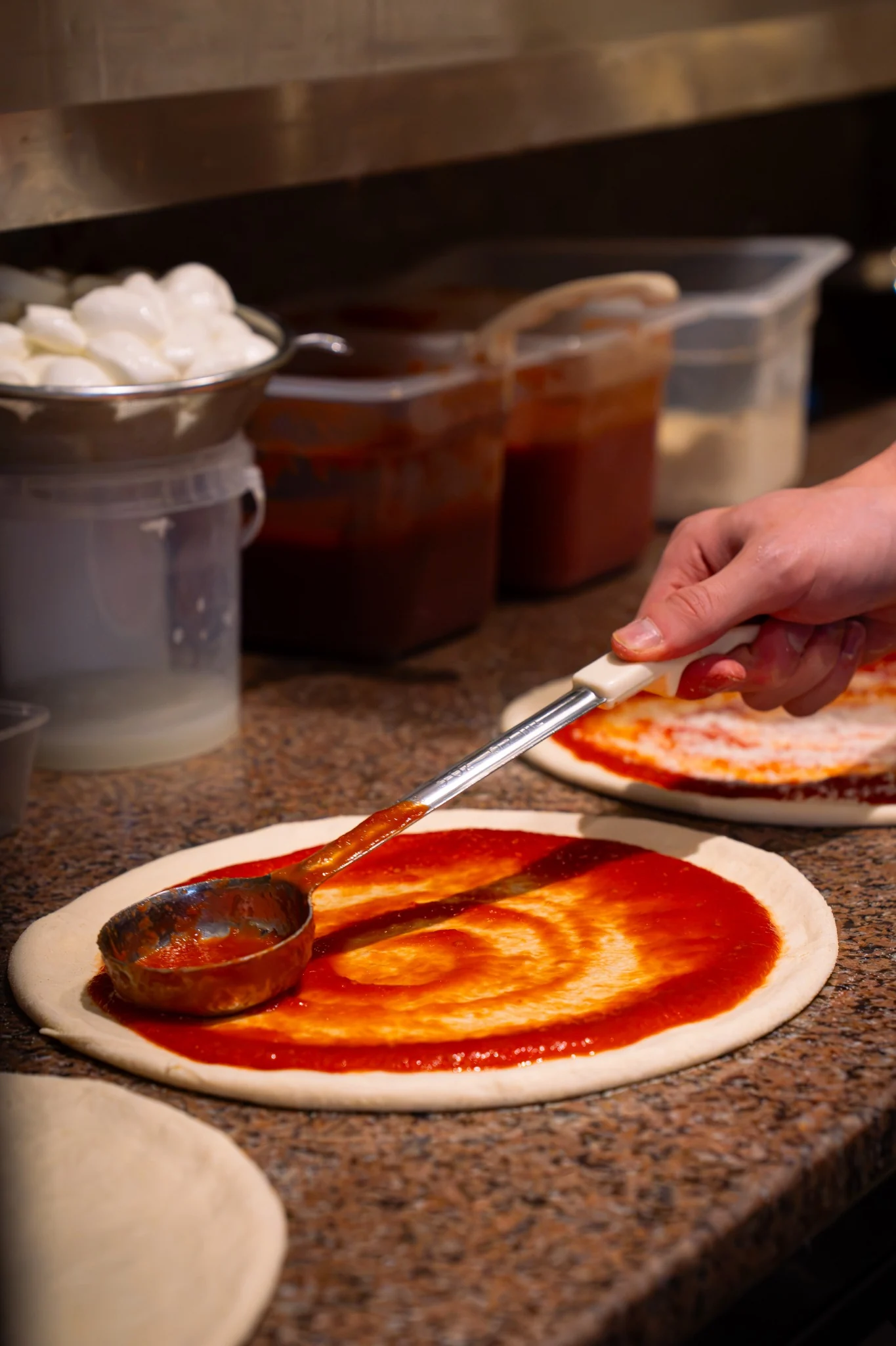 Tomato sauce being spread over fresh pizza dough at Billy’s Pizza