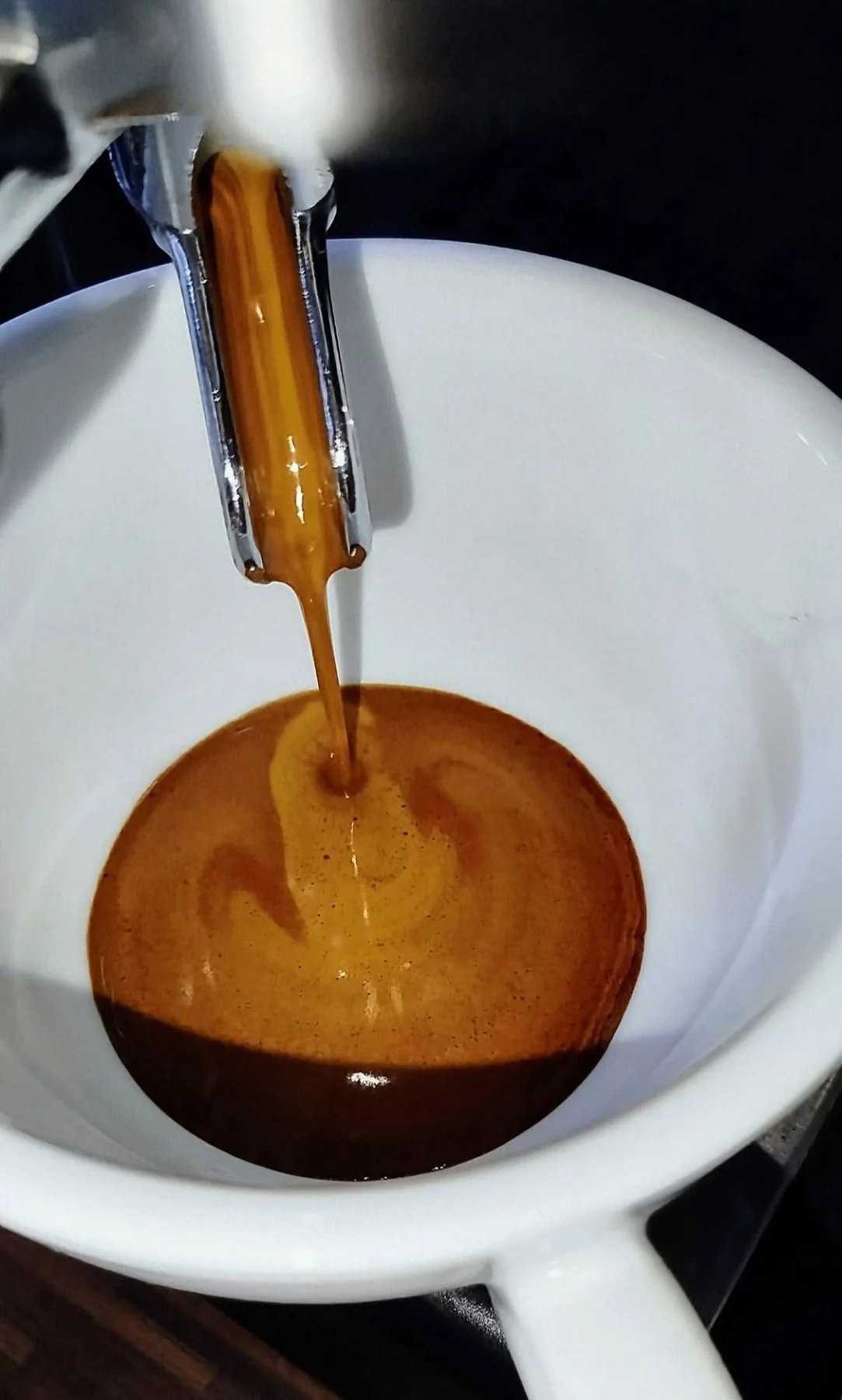 Close detail of espresso being extracted into a white cup