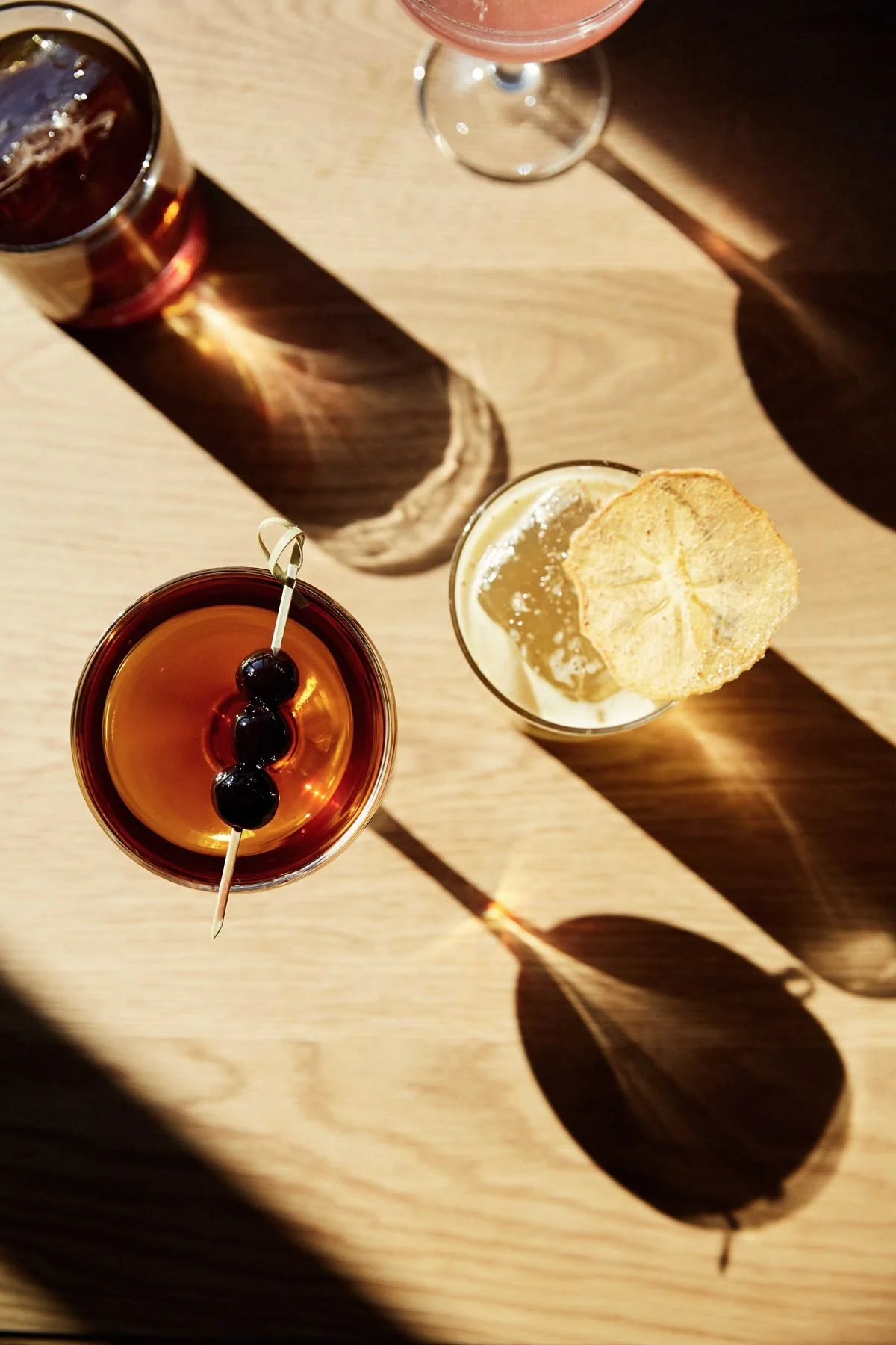 Cocktails casting long graphic shadows across a sunlit wooden table