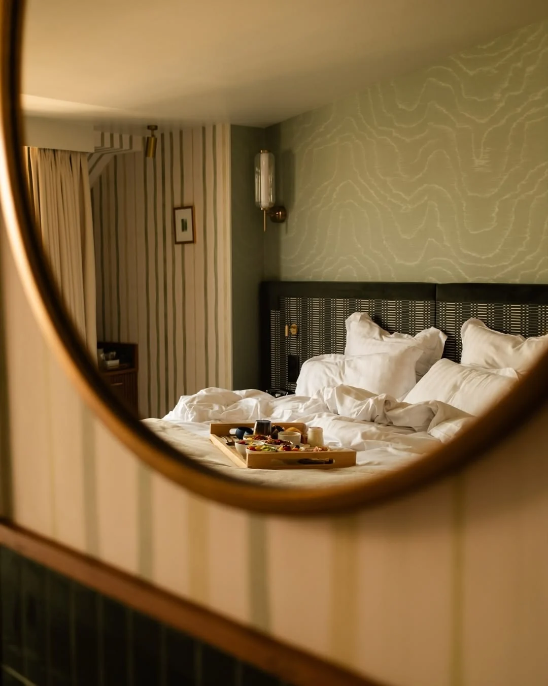 Warm hotel bedroom with breakfast tray reflected in a round mirror