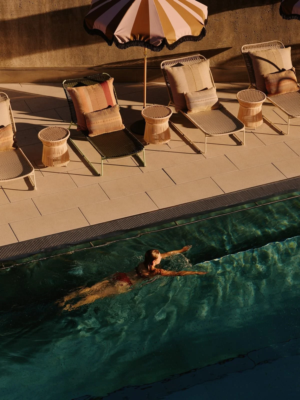 Swimmer in a sunlit hotel pool surrounded by loungers on Isola di San Pietro in Sardinia