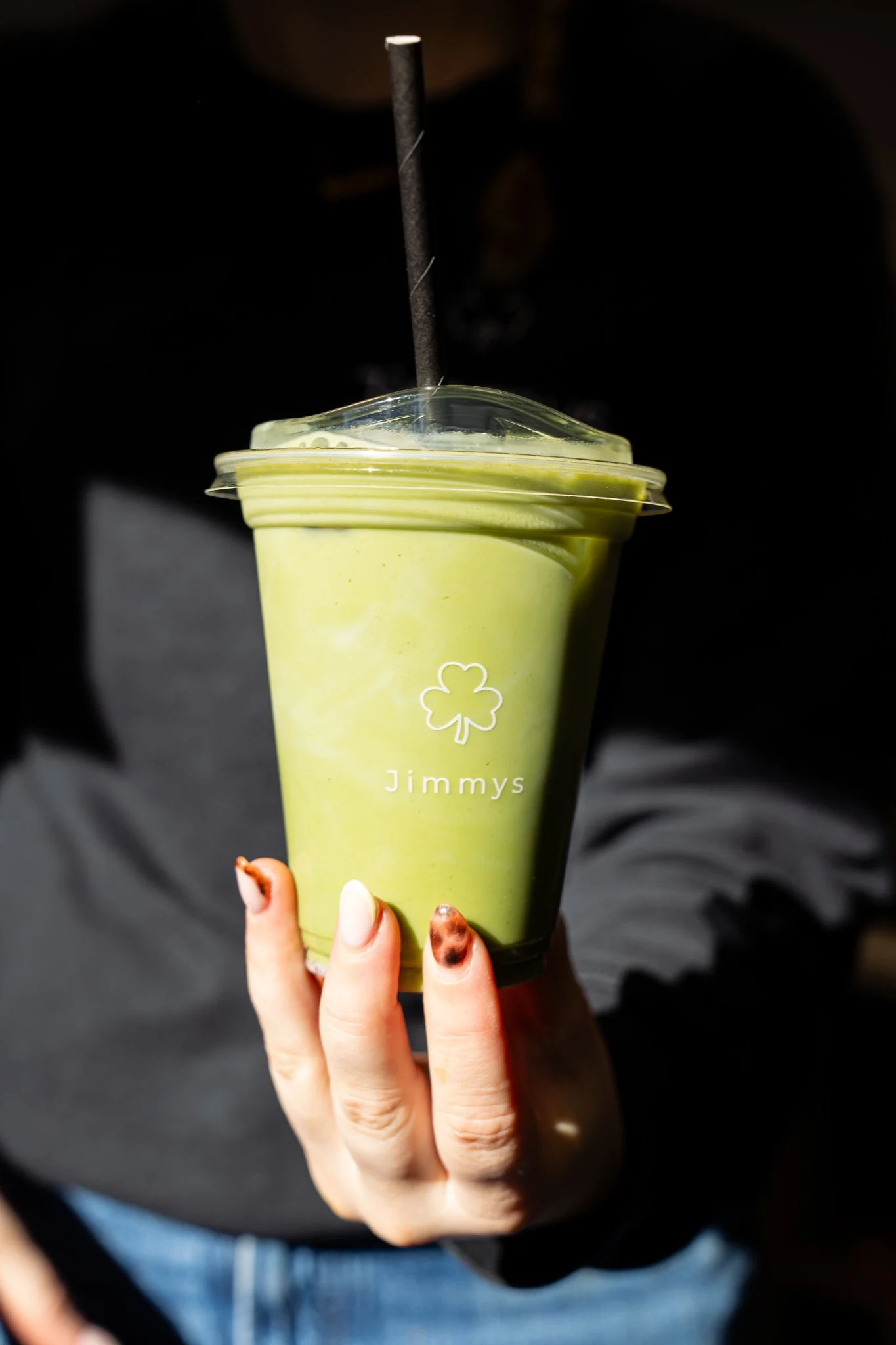 Green smoothie held in dramatic sunlight with Jimmy’s branding