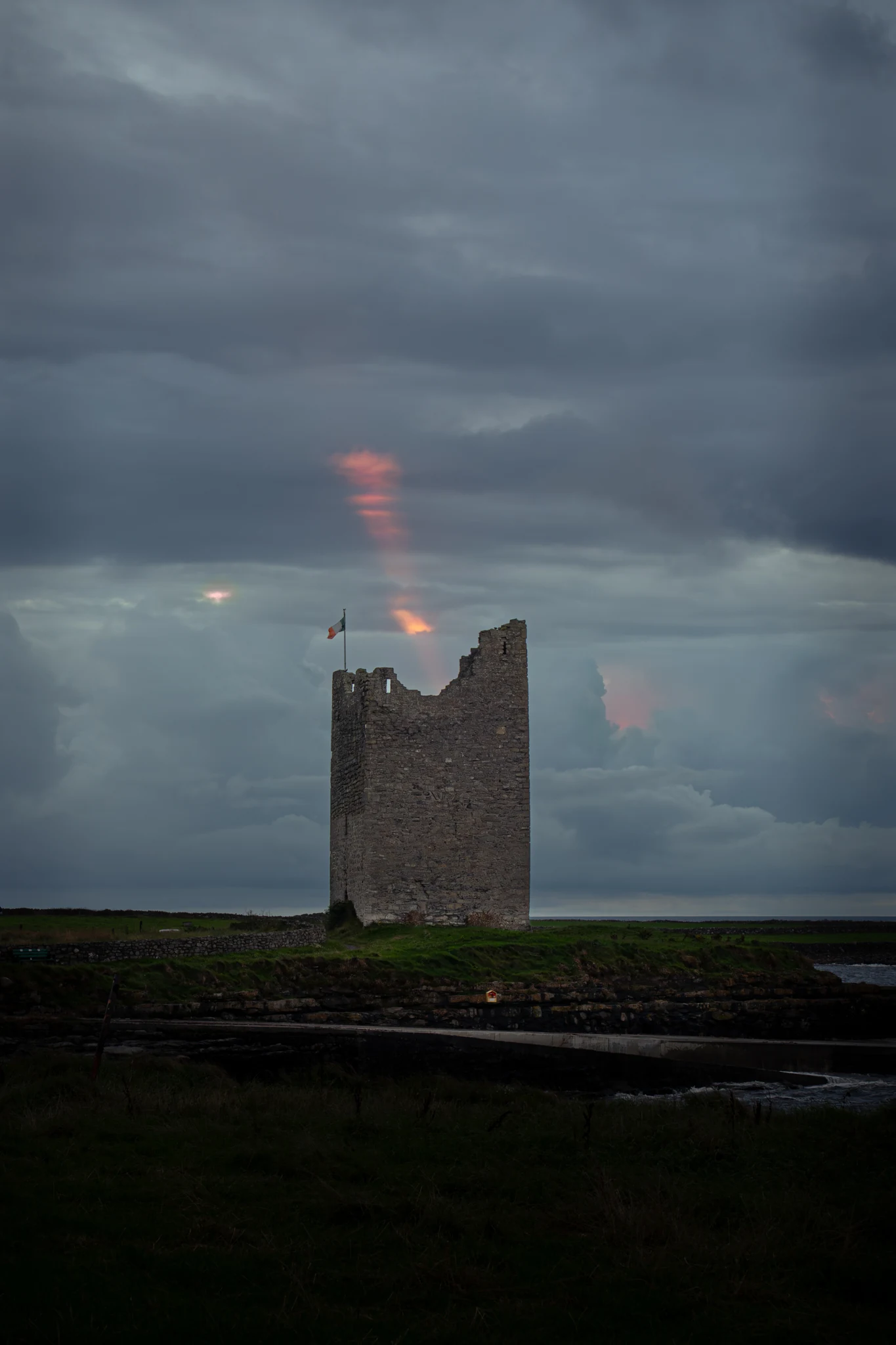 Historic stone tower on the Irish coast beneath storm clouds and a glowing rainbow