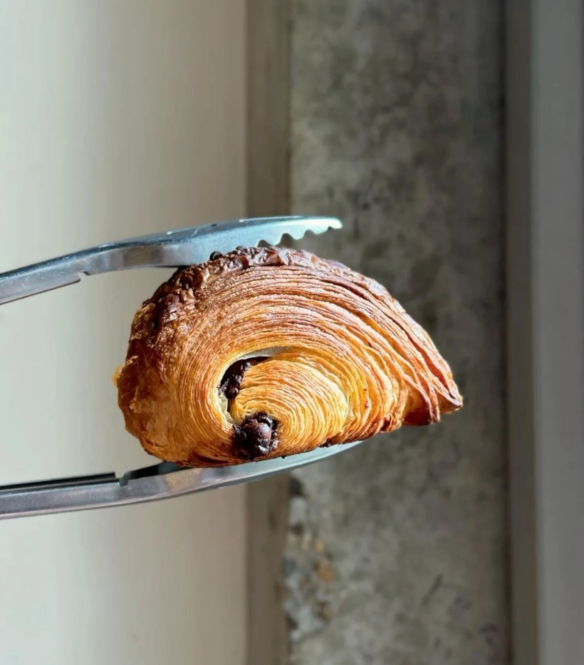 Flaky pain au chocolat held with pastry tongs