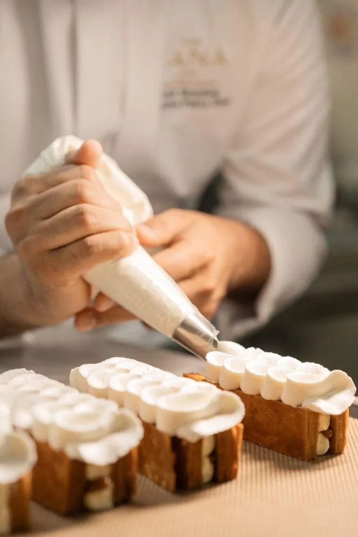 Pastry chef piping cream onto baked goods